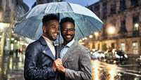 Two men holding an umbrella in the rain outdoors in the city, romantic gay couple scene