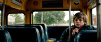 A concerned-looking teenager standing beside a yellow school bus, cinematic look, wide horizontal